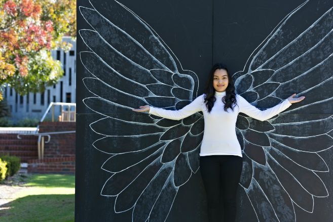 Campus female raising arms against wall