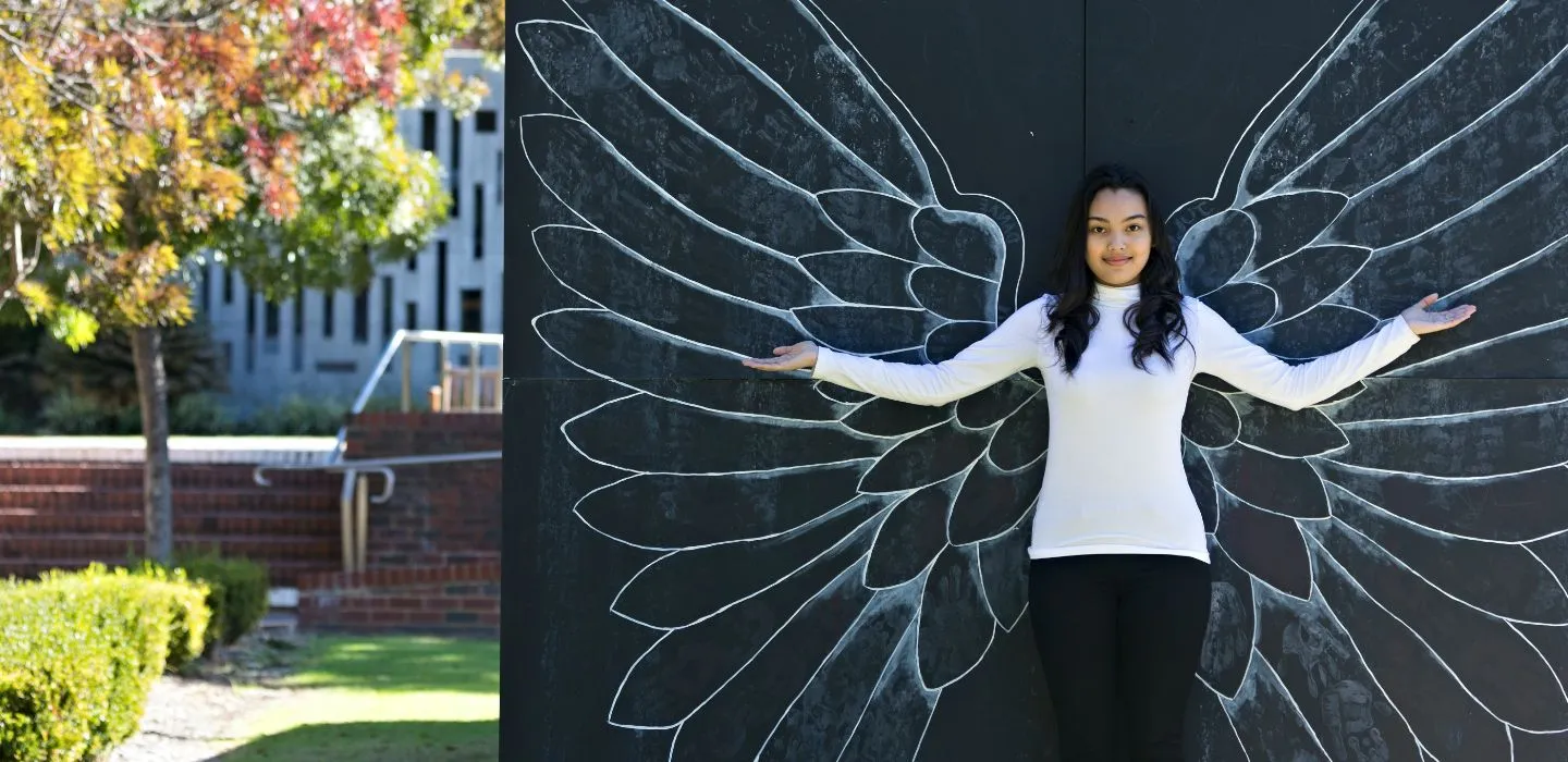 Campus female raising arms against wall